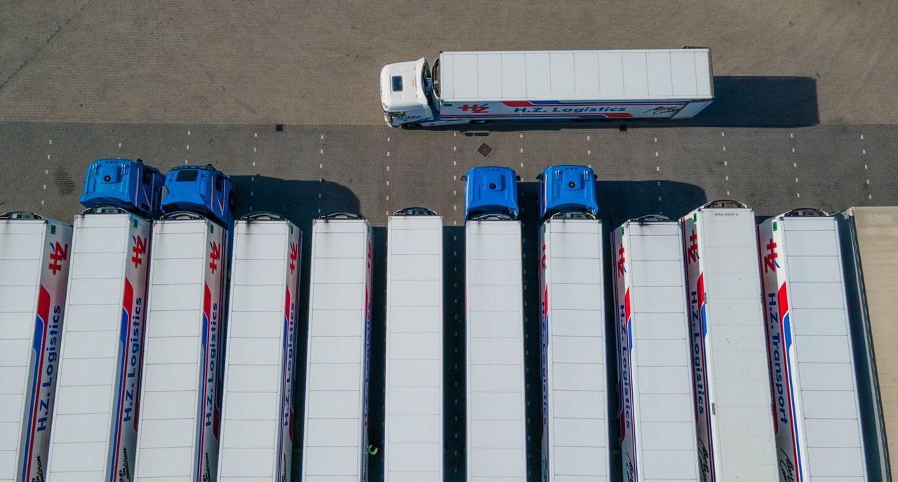gallery-6 Top-down drone shot of logistics trucks arranged in a row in a parking lot.