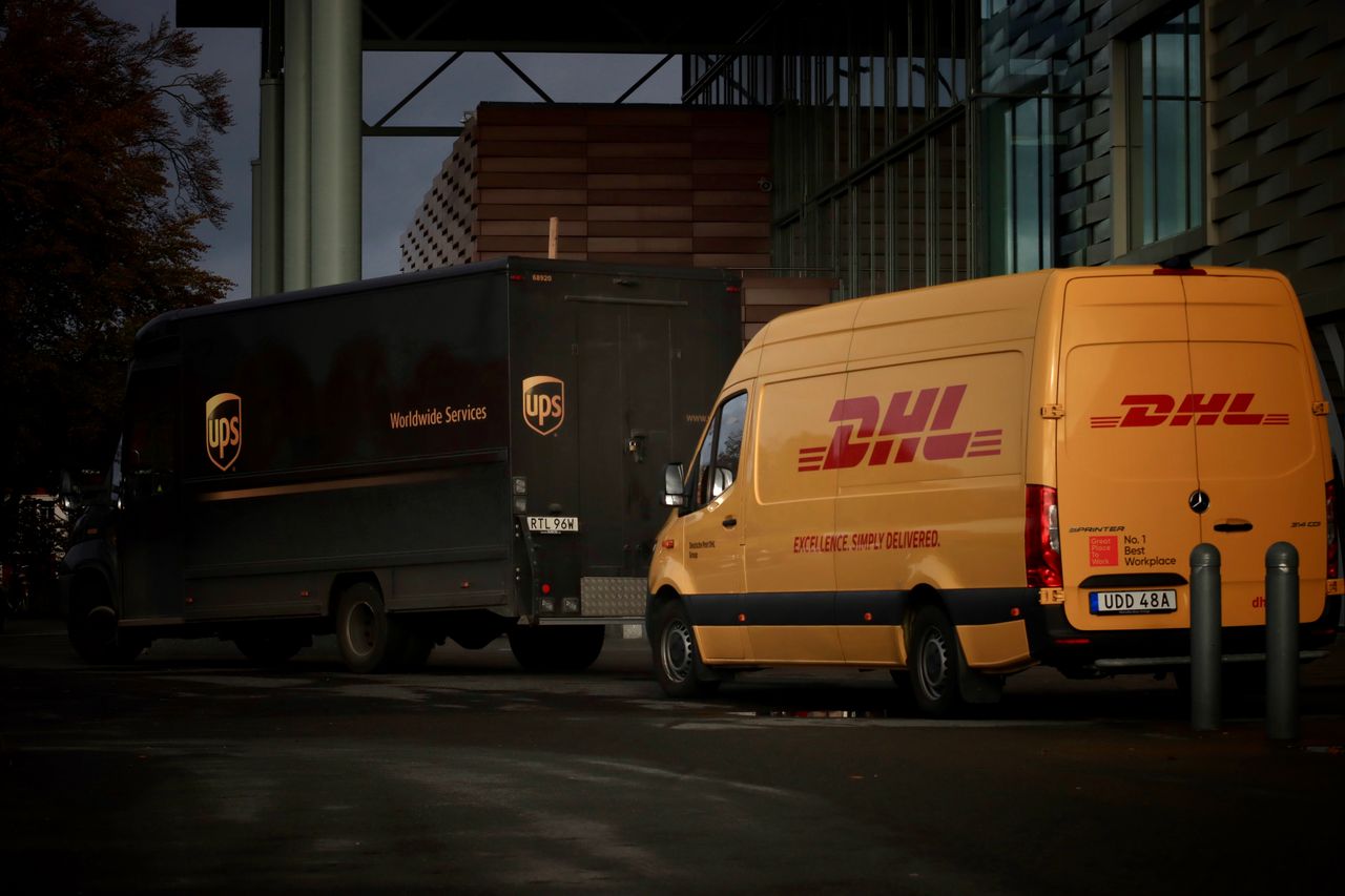gallery-4 DHL and UPS delivery trucks parked at night near a modern building, ready for logistics operations.