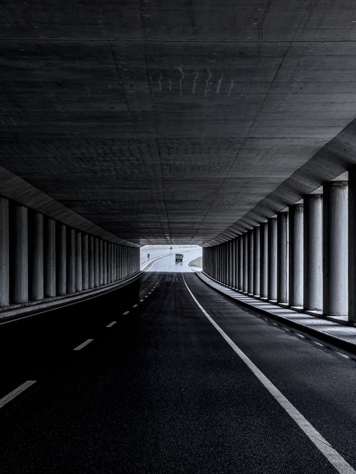 Dark urban tunnel with symmetrical columns and road leading to the light.