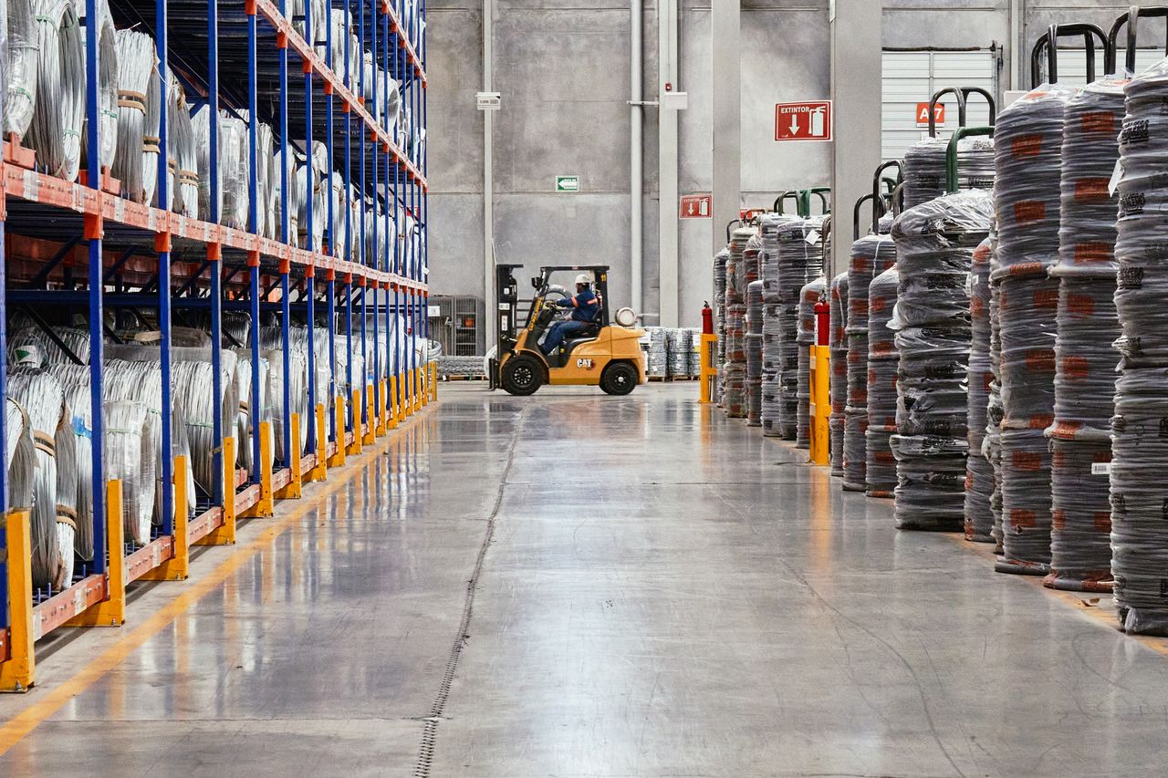 why-choose-us A forklift operates in an industrial warehouse with stacked goods. Efficient distribution setting.