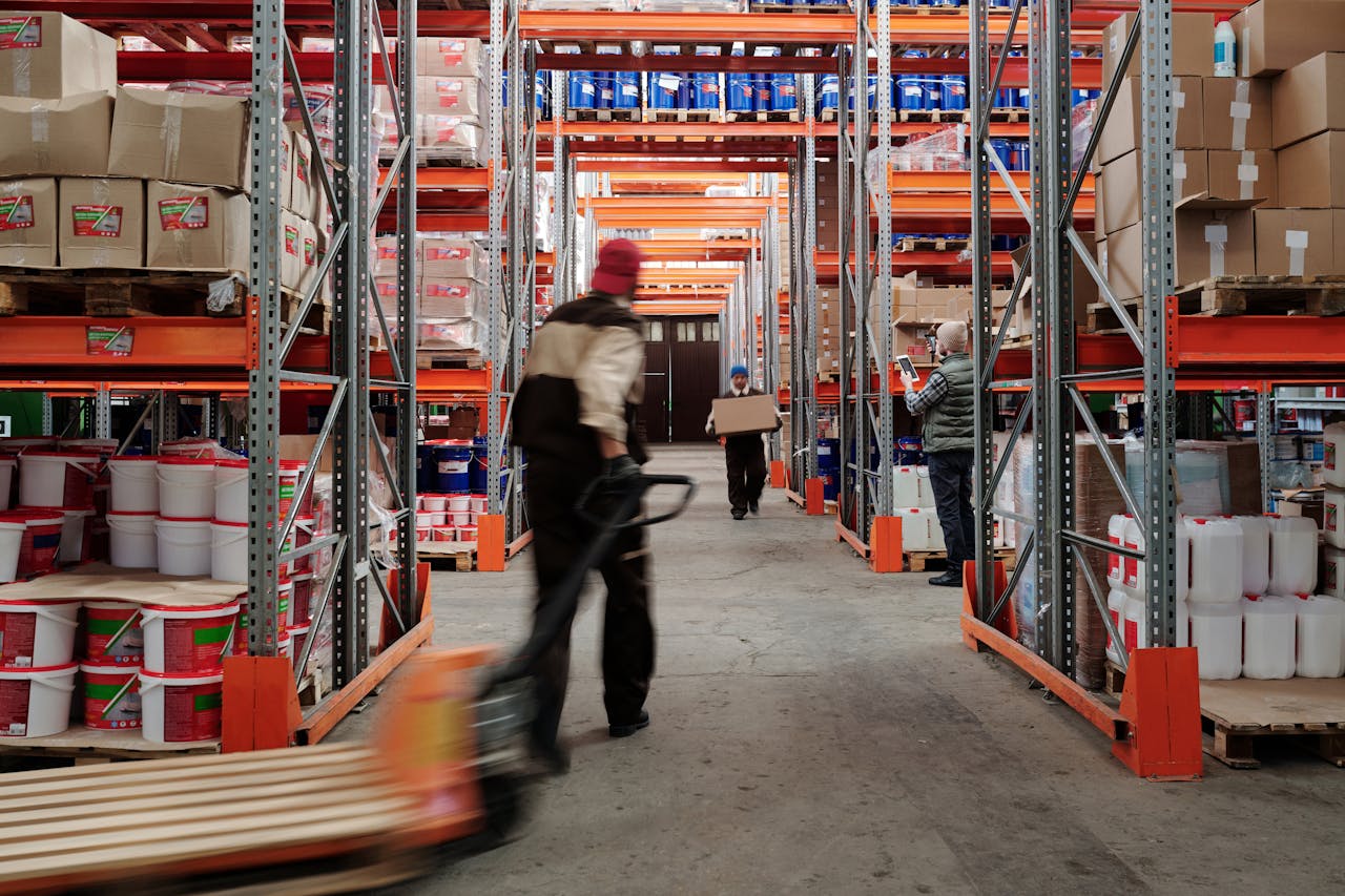 hero-img-01 Warehouse interior with workers organizing shelves full of boxes and containers.