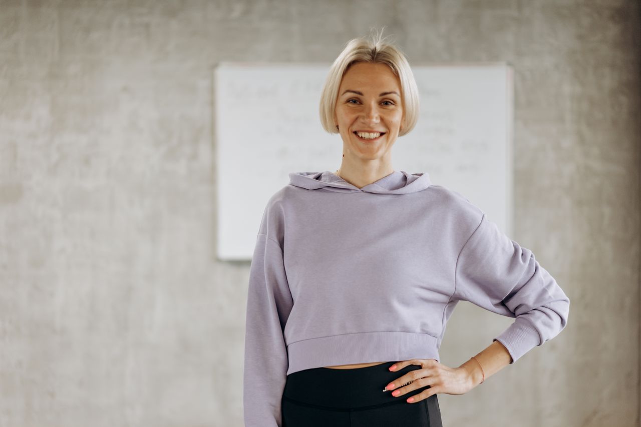 Happy woman in fitness wear poses confidently indoors, promoting healthy lifestyle and exercise.